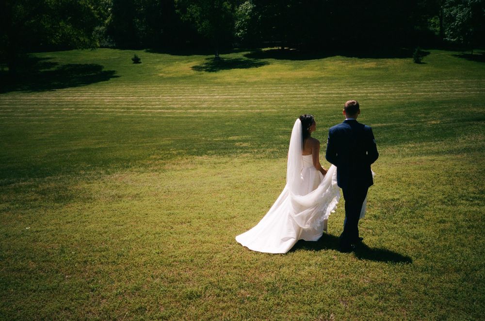 Couple walking across sunny meadow in wedding attire.