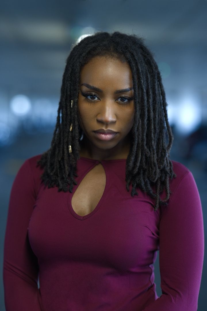 A person wearing a burgundy long-sleeve top with a keyhole neckline and locs hairstyle poses against a blurred background.