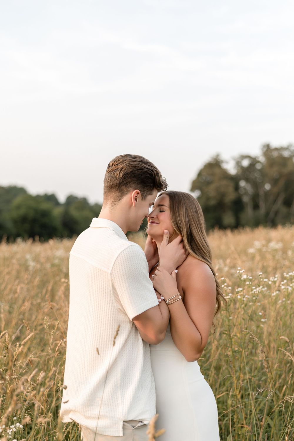 A romantic couple embracing in a sunlit meadow with golden wildflowers and trees in the background.
