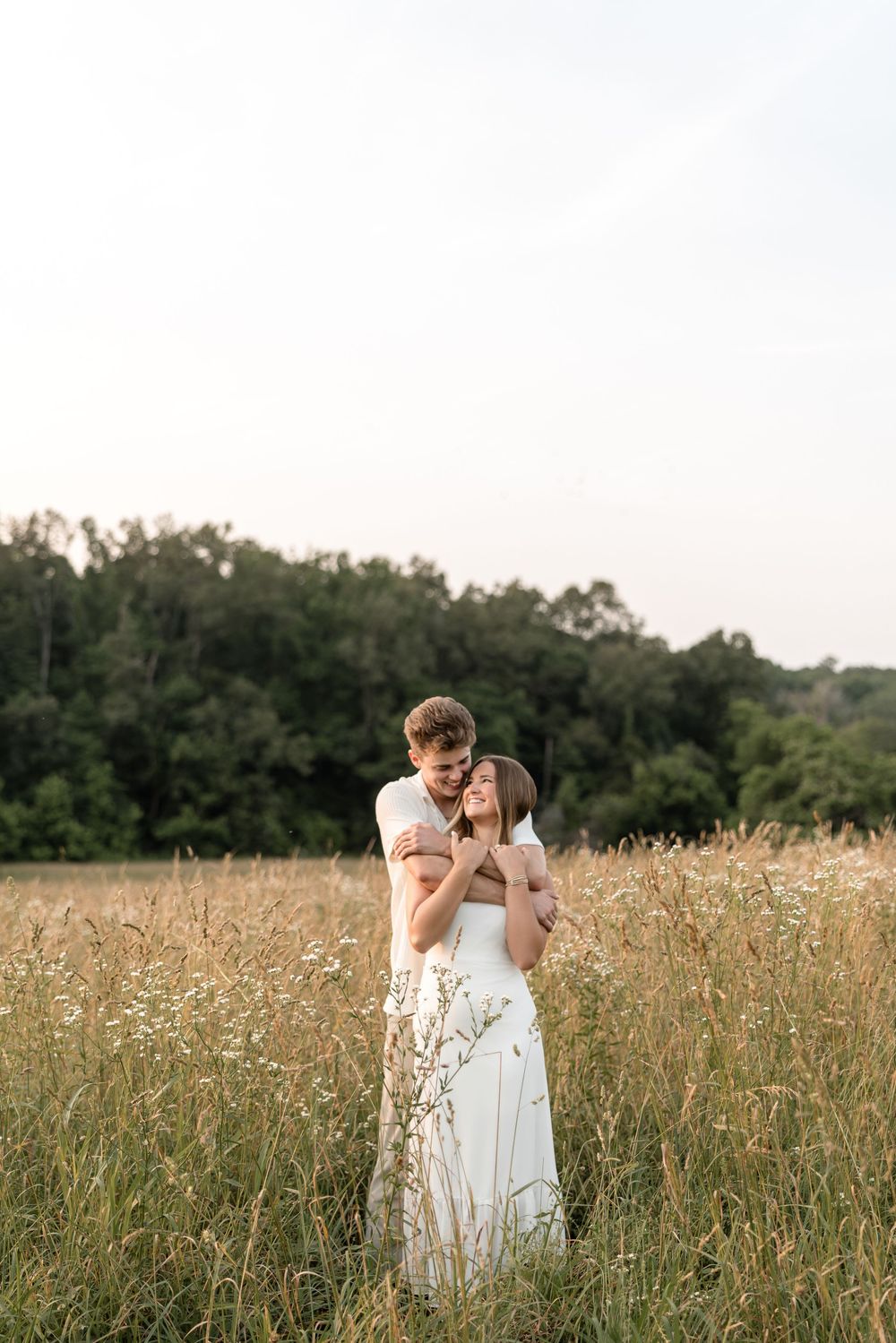 Loving couple embraces in tall summer grass field at golden hour.