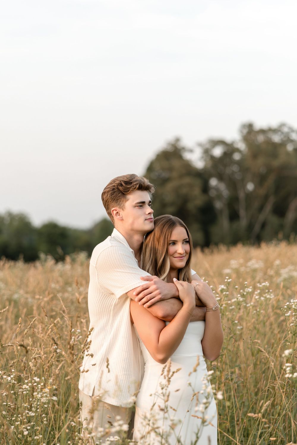 A tender embrace captured in a sunlit meadow filled with wildflowers and tall grass.