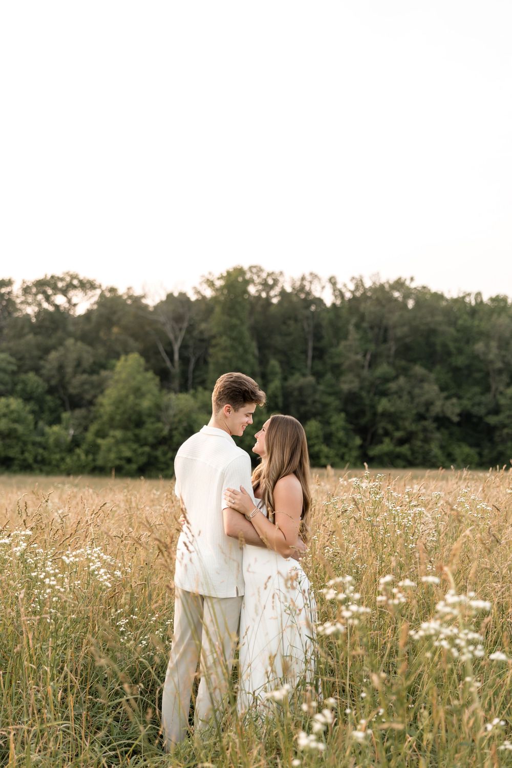 A romantic couple shares an intimate moment while standing in a golden field of wildflowers at dusk.