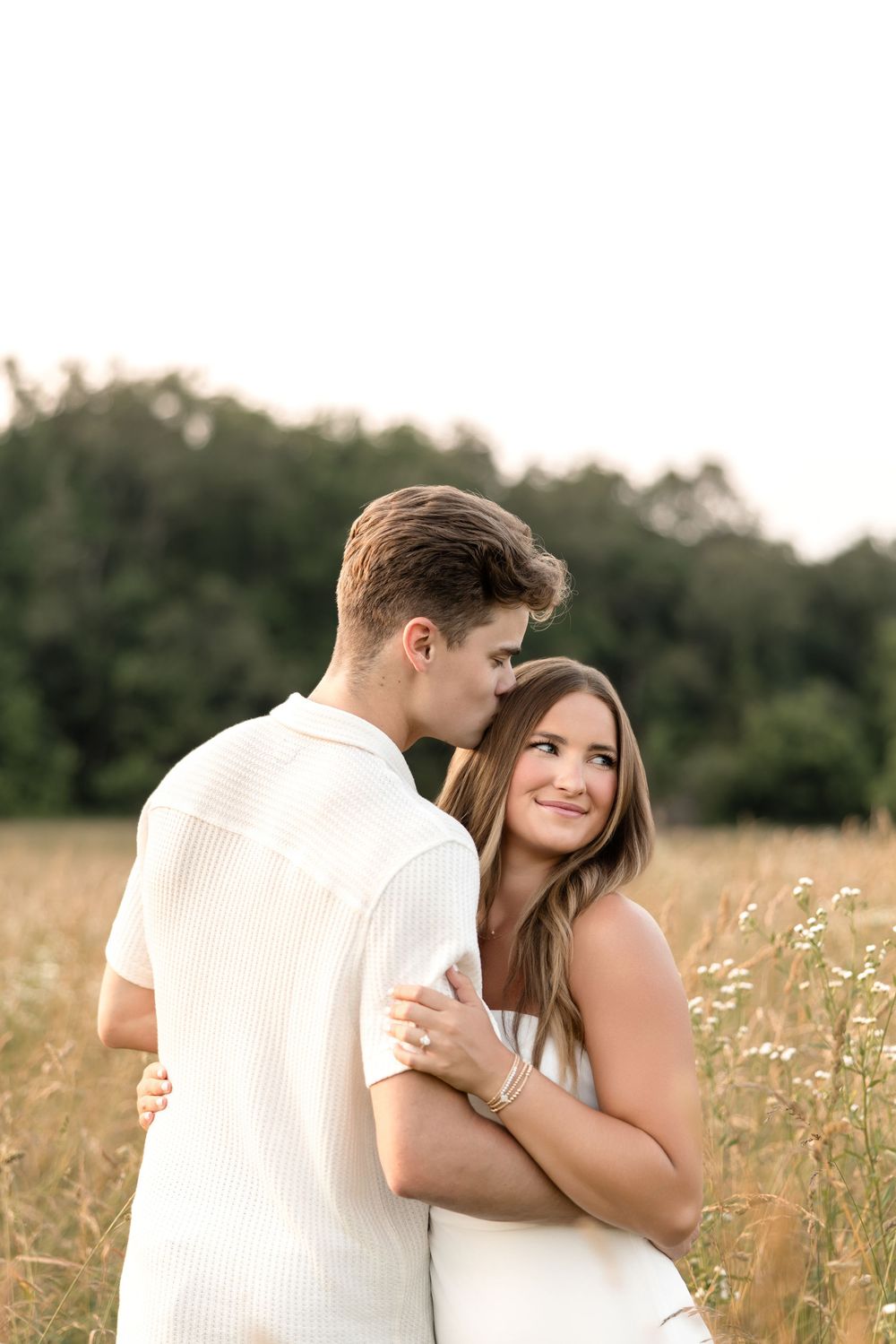 Sweet moment between couple in white clothing standing together in a golden field.