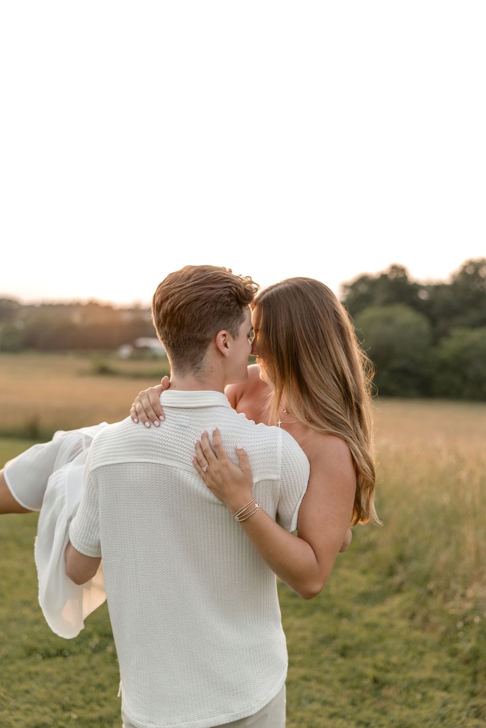A romantic couple shares an intimate moment in a golden field at sunset.