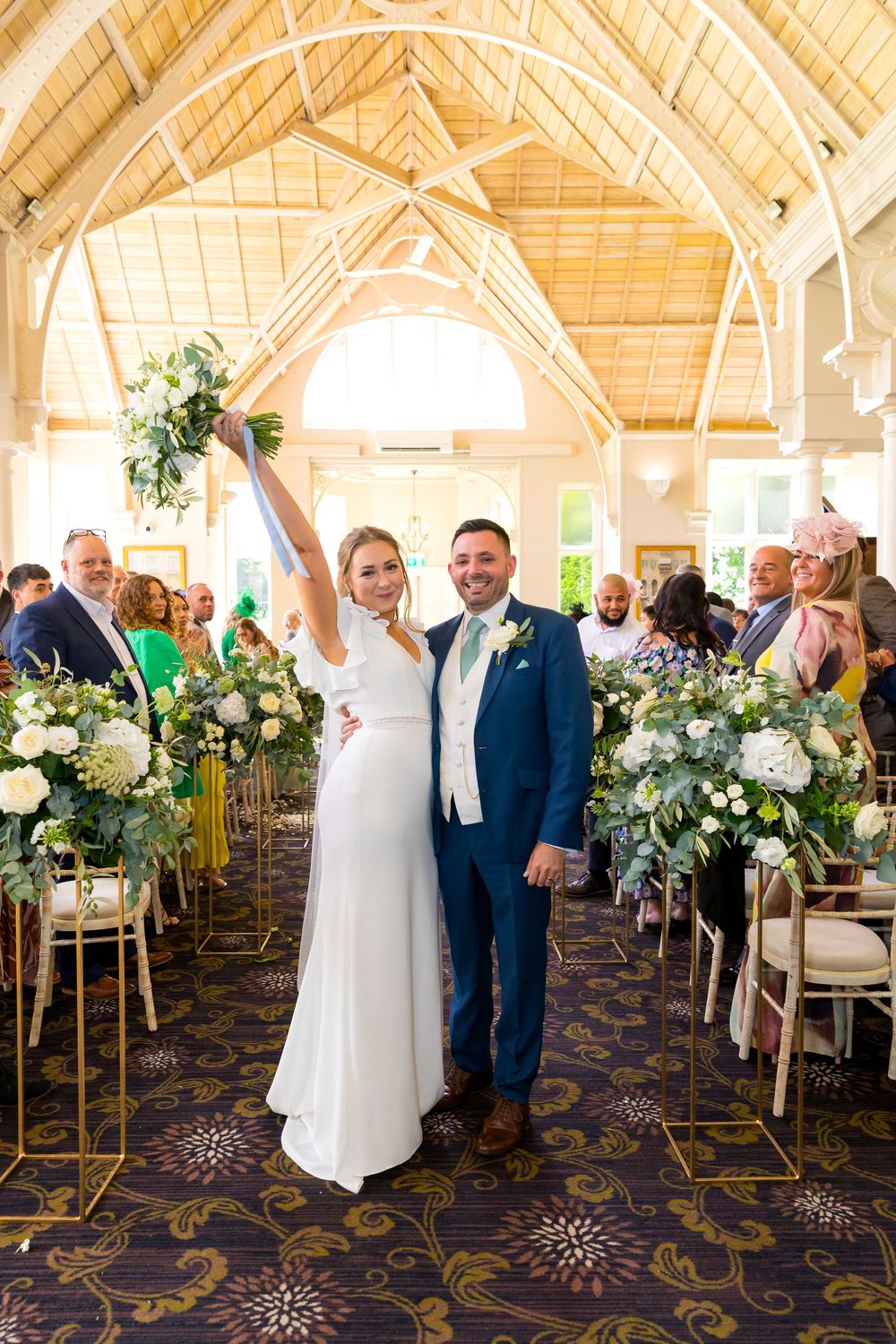 Louisa and Alan celebrating as newlyweds, standing proudly in the ceremony room aisle.