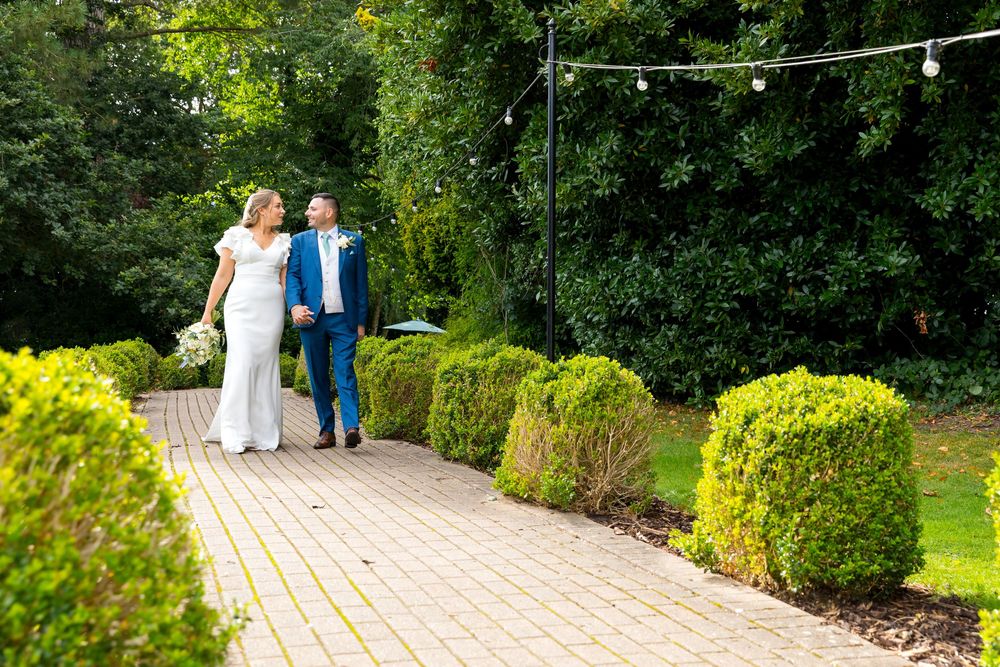 Bride and groom walking hand-in-hand down a garden path