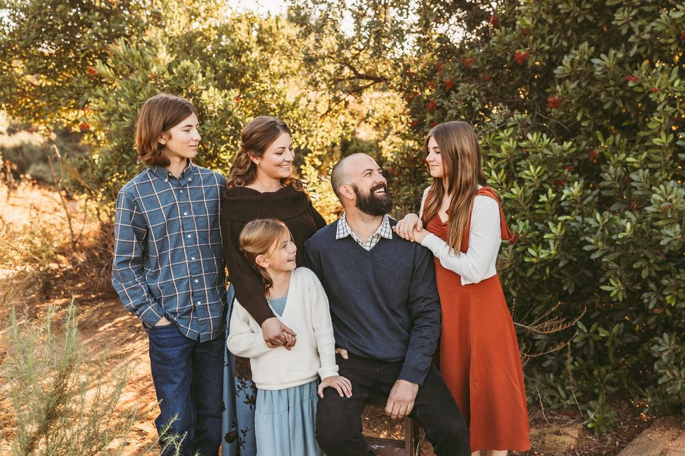 A group of people share laughter and smiles while standing together on a sunlit nature path during golden hour.