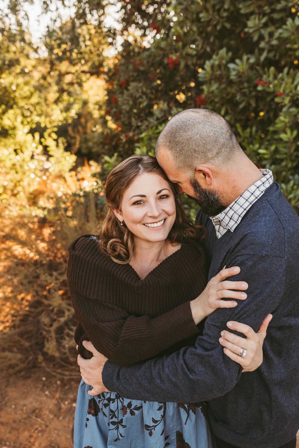 A couple embraces intimately while sharing a joyful moment in golden sunlight with autumn foliage in the background.