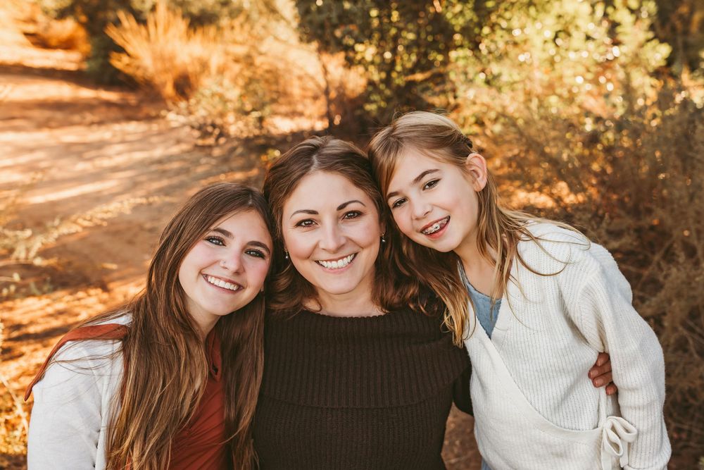 Three people sharing warm smiles together outdoors during golden hour autumn photography session.