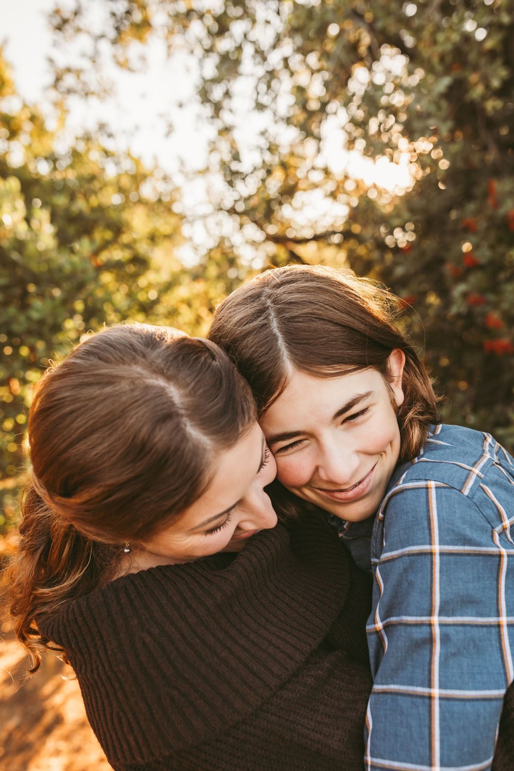 A couple shares a tender laughing moment together during a sunset photoshoot surrounded by trees.