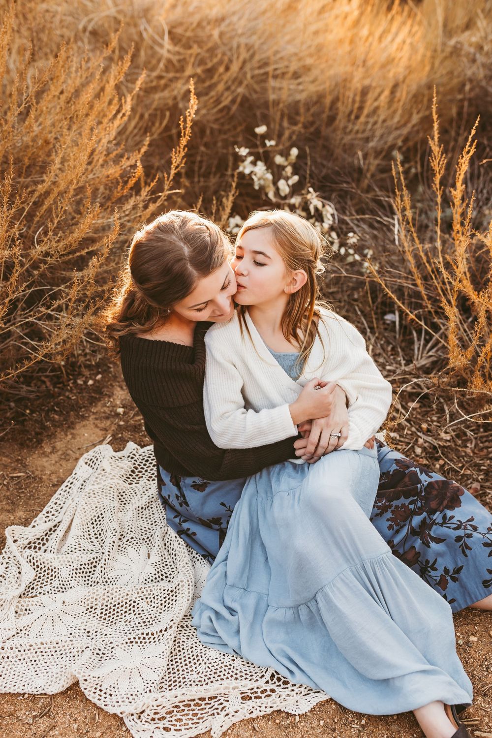 People sitting on lace blankets sharing an intimate moment surrounded by golden dried grass at sunset.
