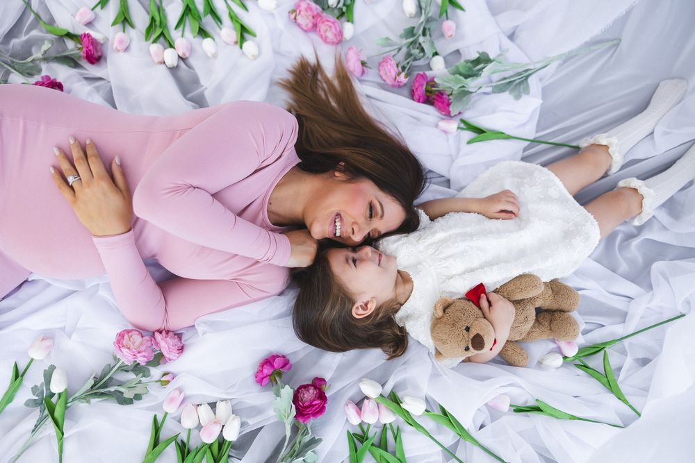 Tender maternity moment captured with pink flowers and white bedding.