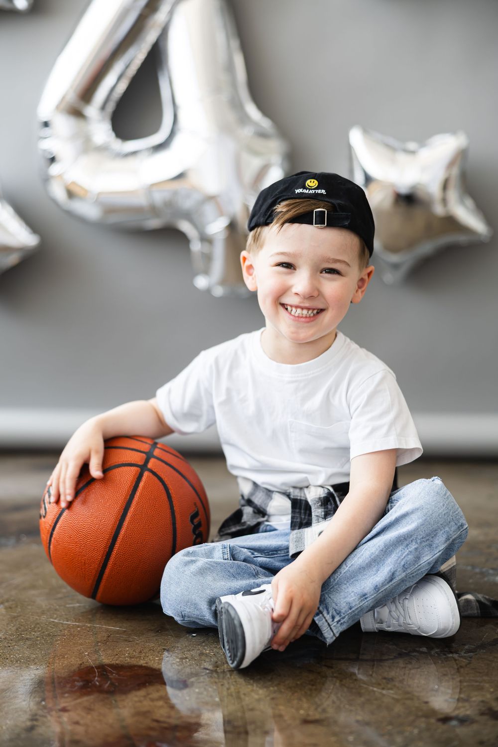 A sequence of photos showing a young child sitting with a basketball on a dark floor with white balloon decorations above.