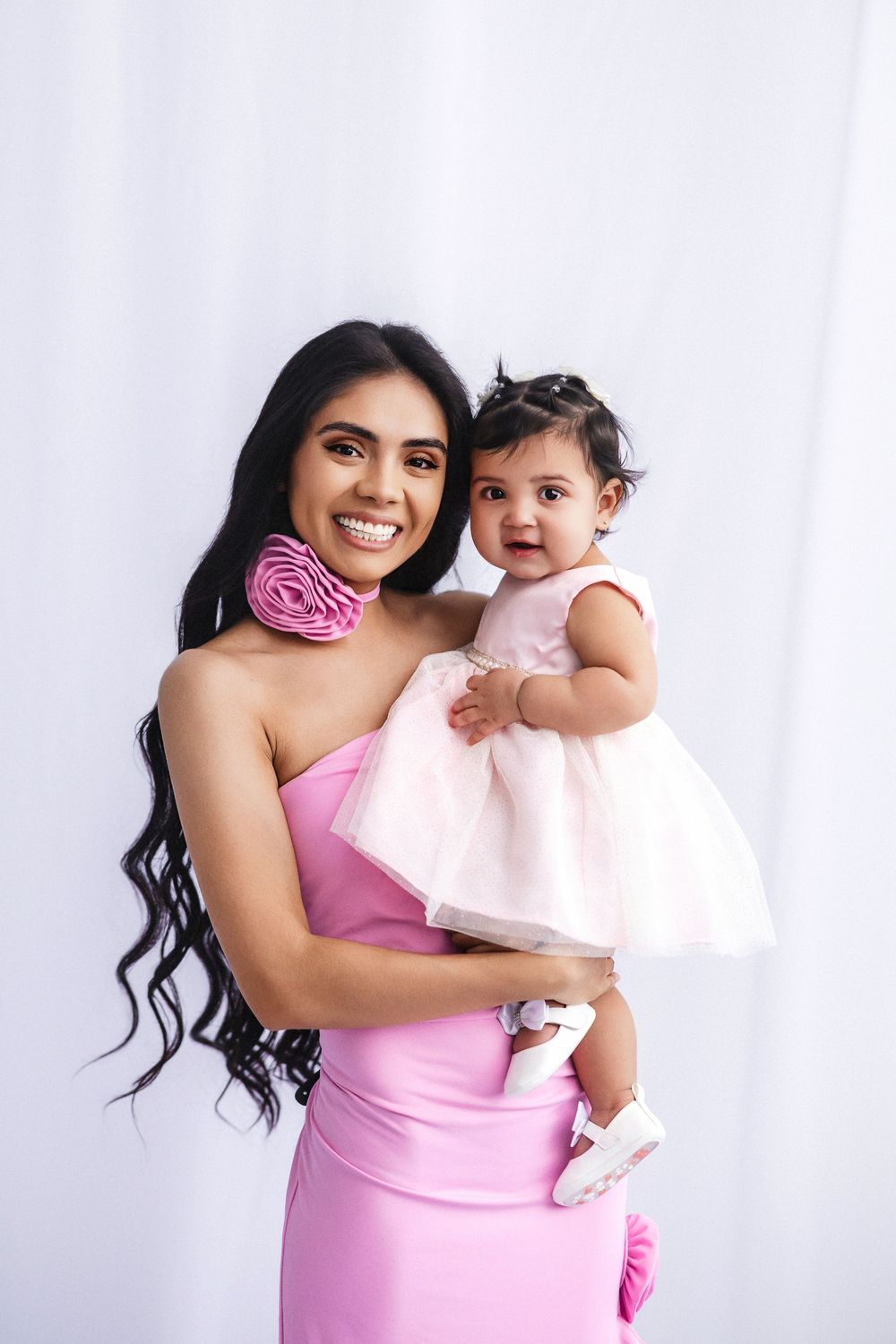 A parent and baby in matching pink attire pose together against a white background.