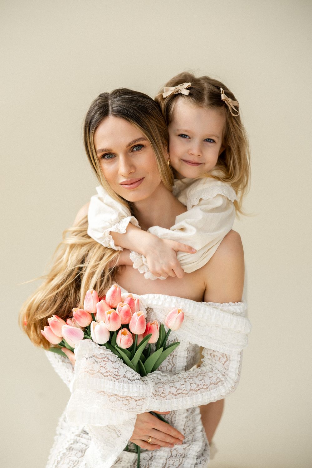 Elegant portrait of parent and child holding pink tulips in white lace dress.