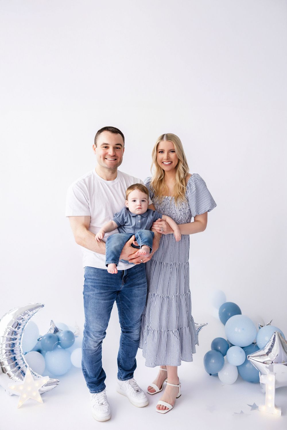 Family portrait with blue balloon decor and white backdrop.