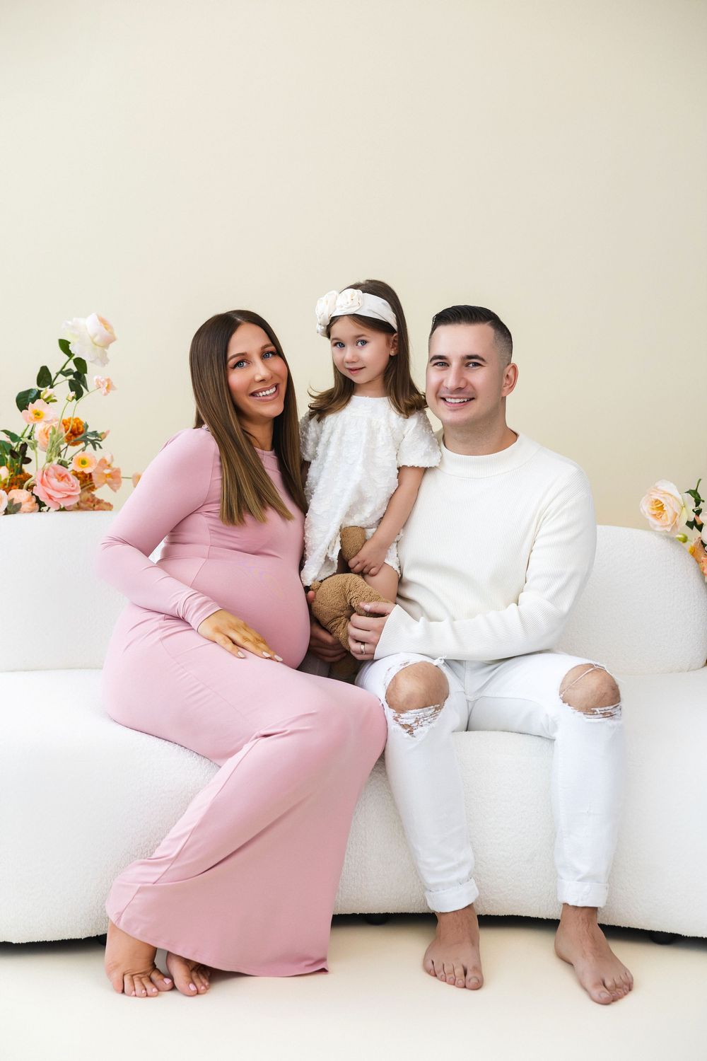 Family portrait on white couch with floral decorations.