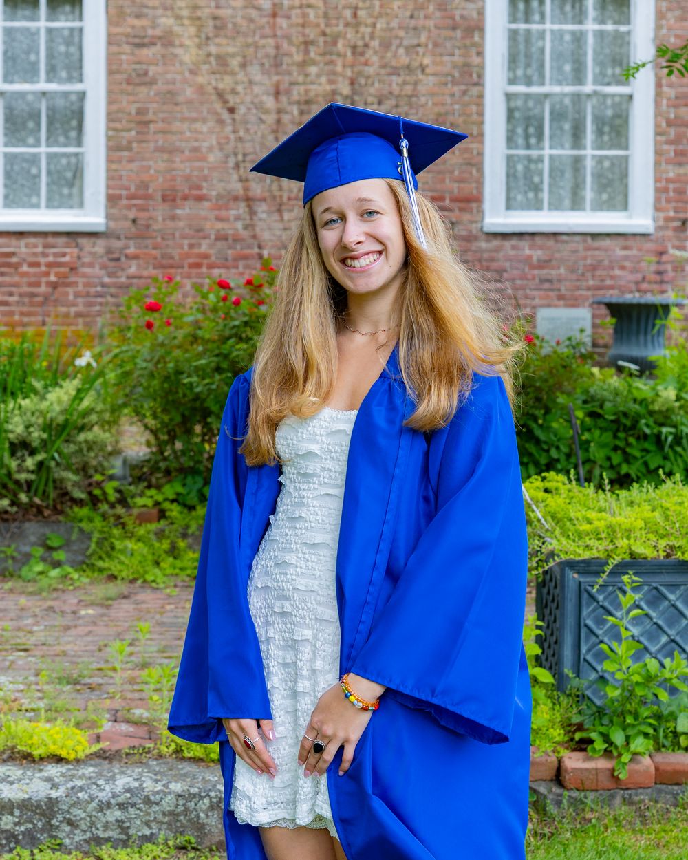 Graduate stands outdoors in traditional blue graduation regalia near a brick building.
