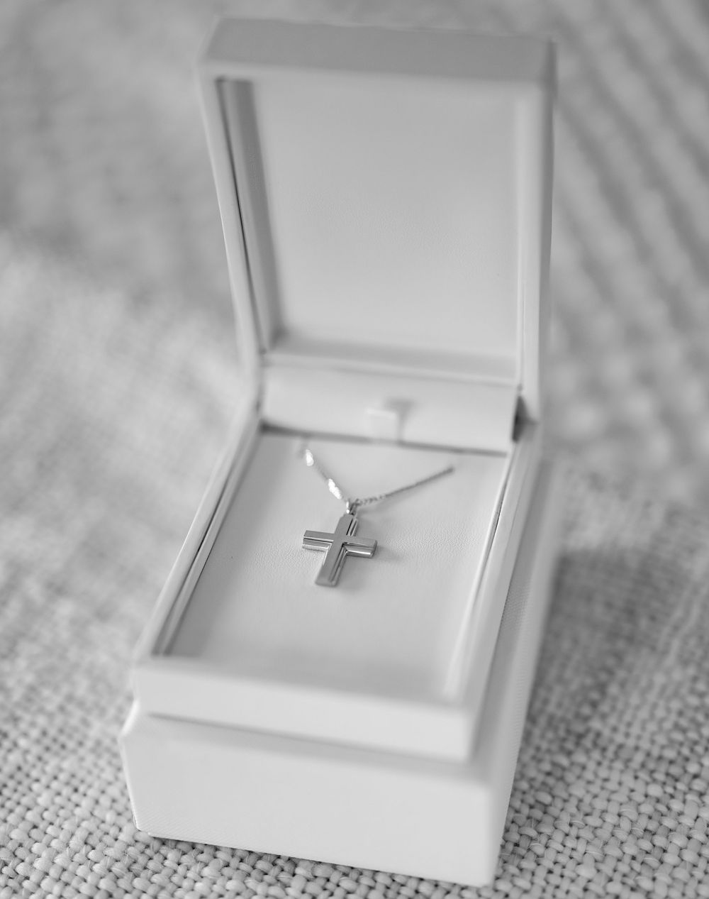 A silver cross necklace pendant displayed in an open white jewelry box.