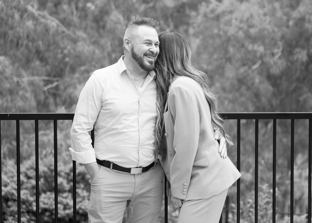 A heartwarming outdoor deck scene showing moment of affection with trees in background, shot in black and white.