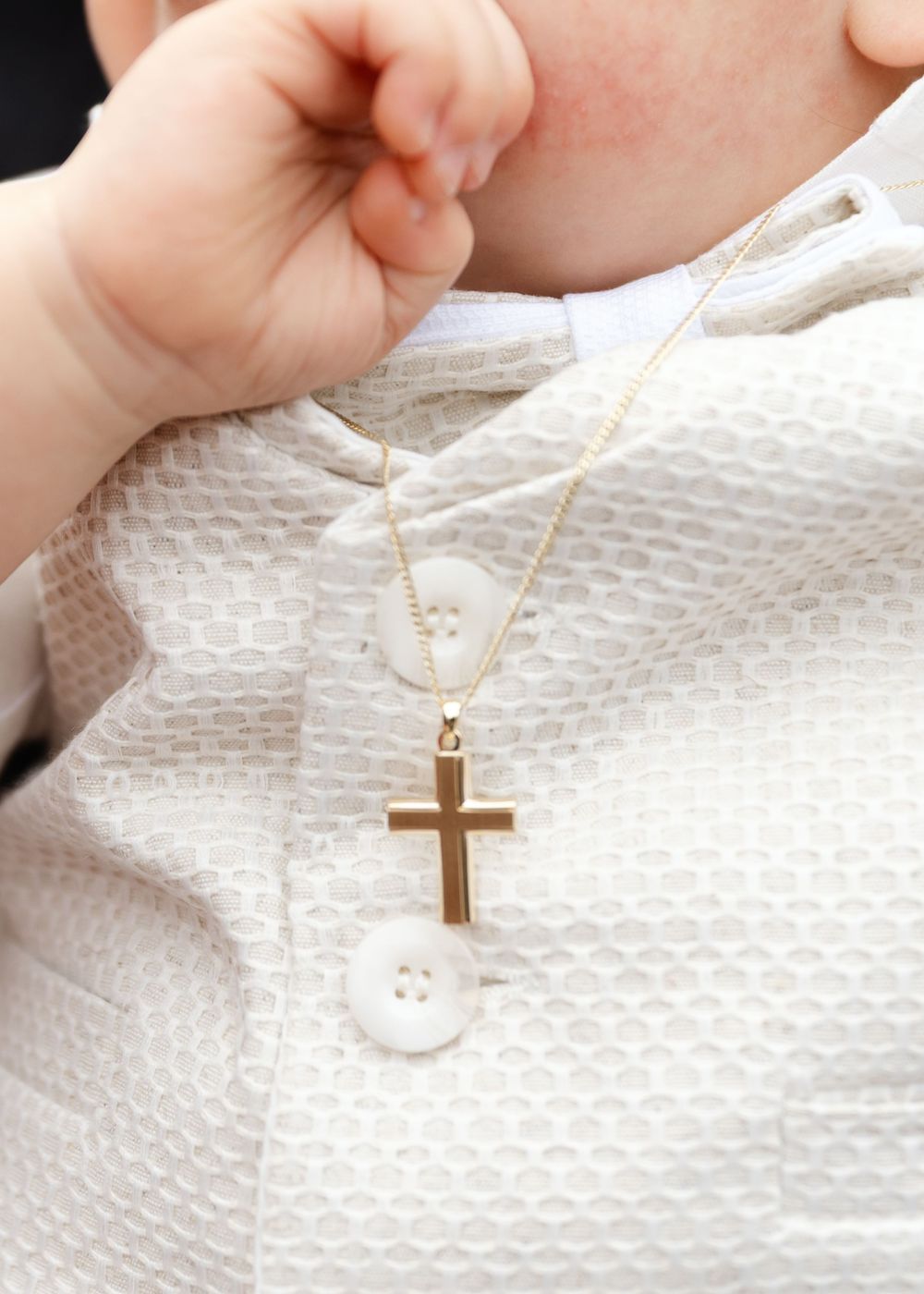 Series of images showing a delicate gold cross necklace being held against white fabric.