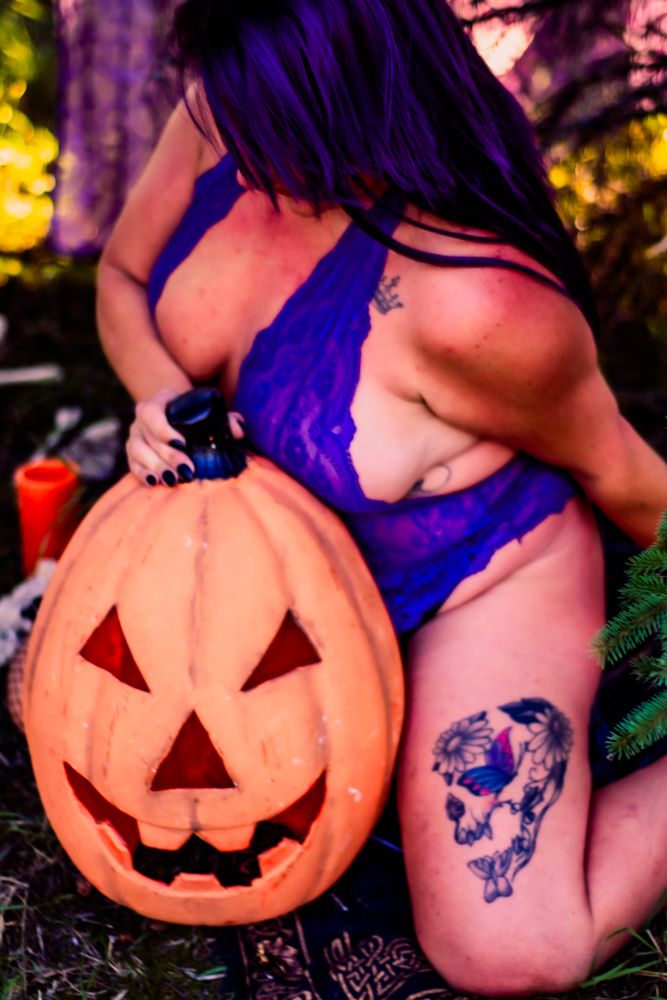 Close up of jack-o-lantern pumpkin with purple decorations in outdoor forest setting.