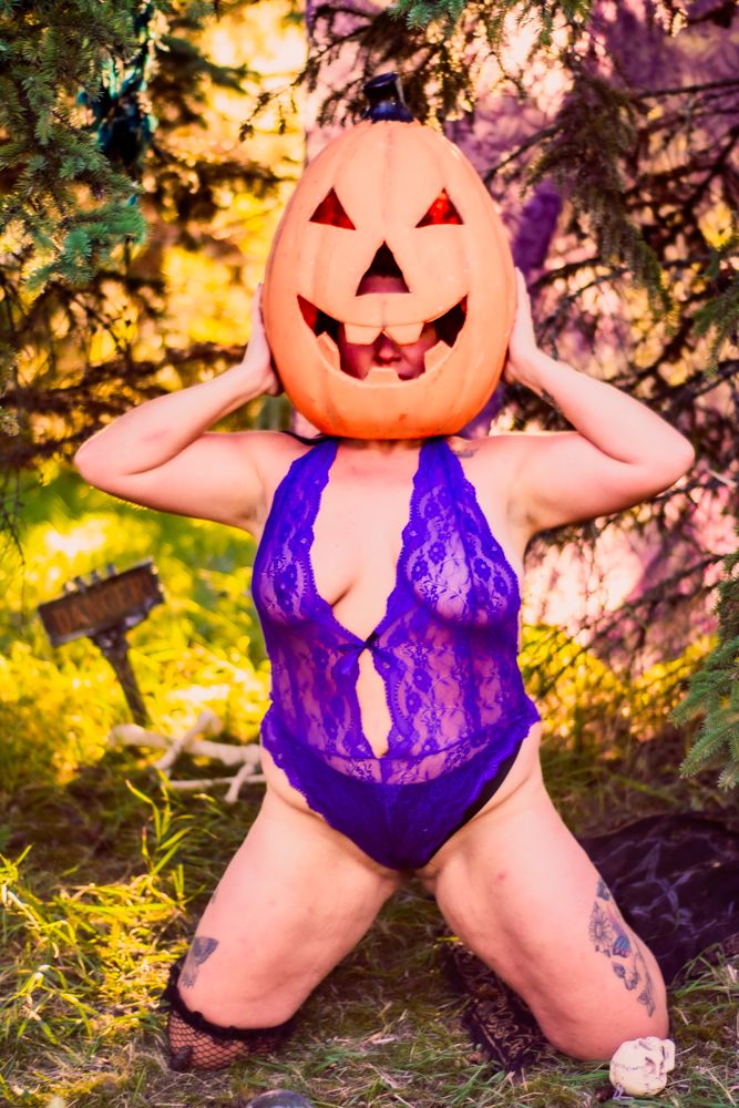 Creative Halloween portrait with jack-o-lantern head and purple bodysuit in autumn forest setting.