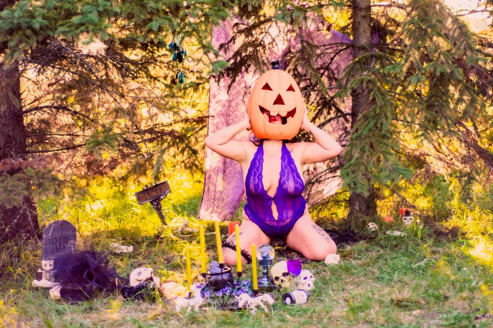 Artistic Halloween scene with carved pumpkin mask and purple costume against golden sunset.