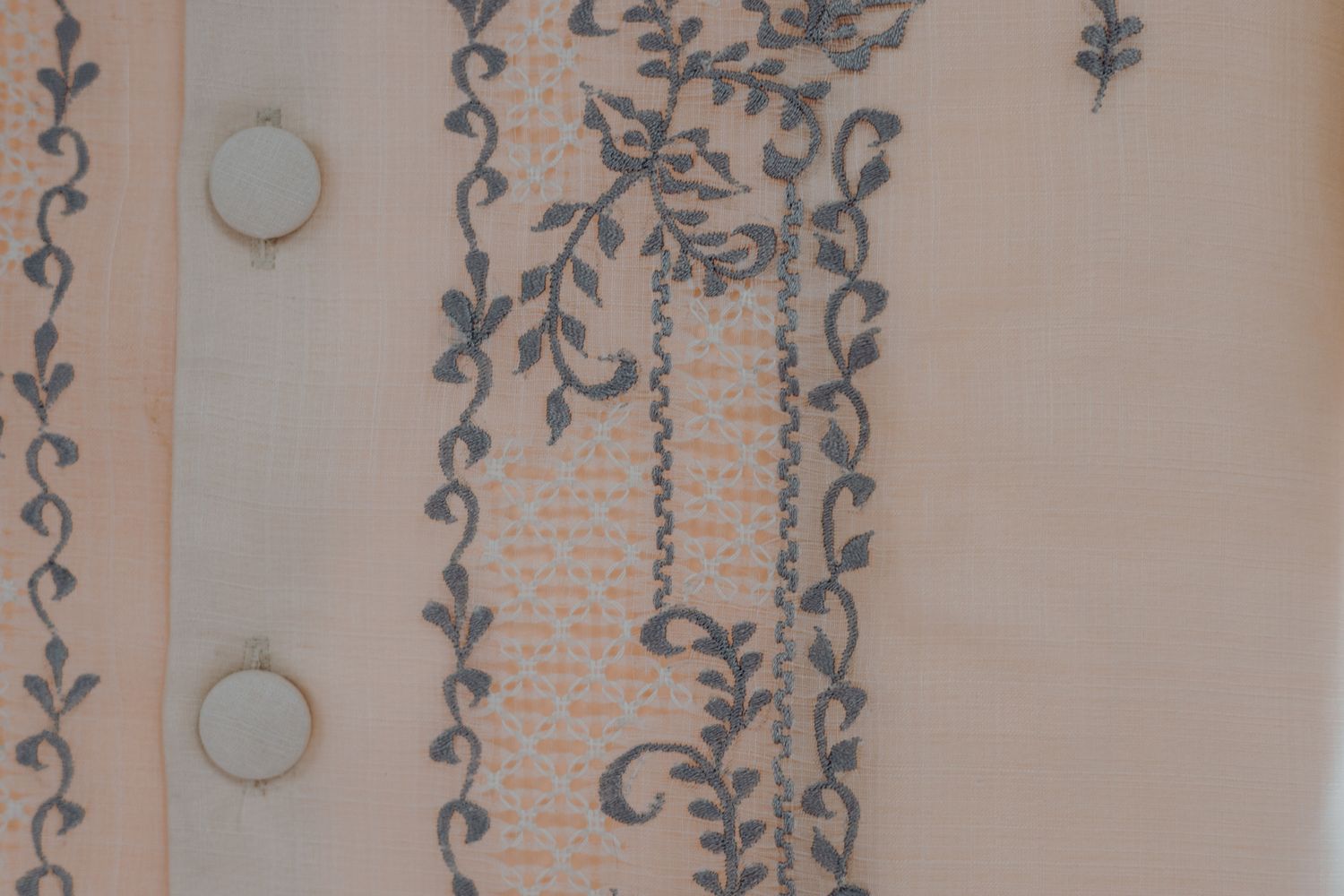 Close-up of delicate floral embroidery pattern on light colored fabric with buttons.