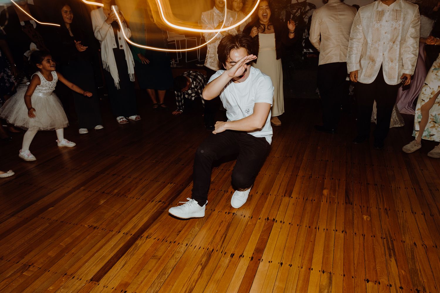 Person performing dance moves on a wooden floor at an indoor celebration.