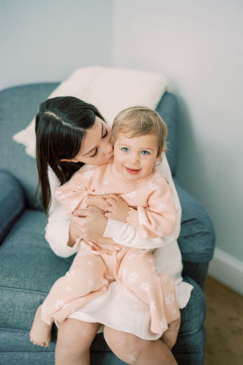 A tender moment between parent and child cuddling on a blue couch in matching pink outfits.