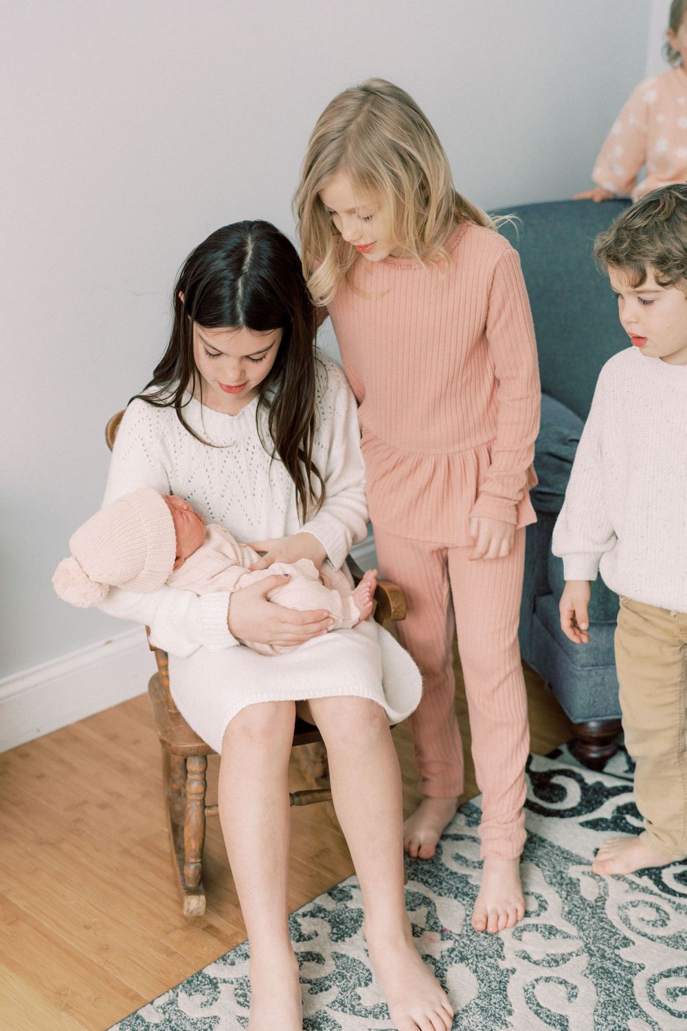 Children gathered around on wooden chair wearing coordinated pink and white winter outfits.