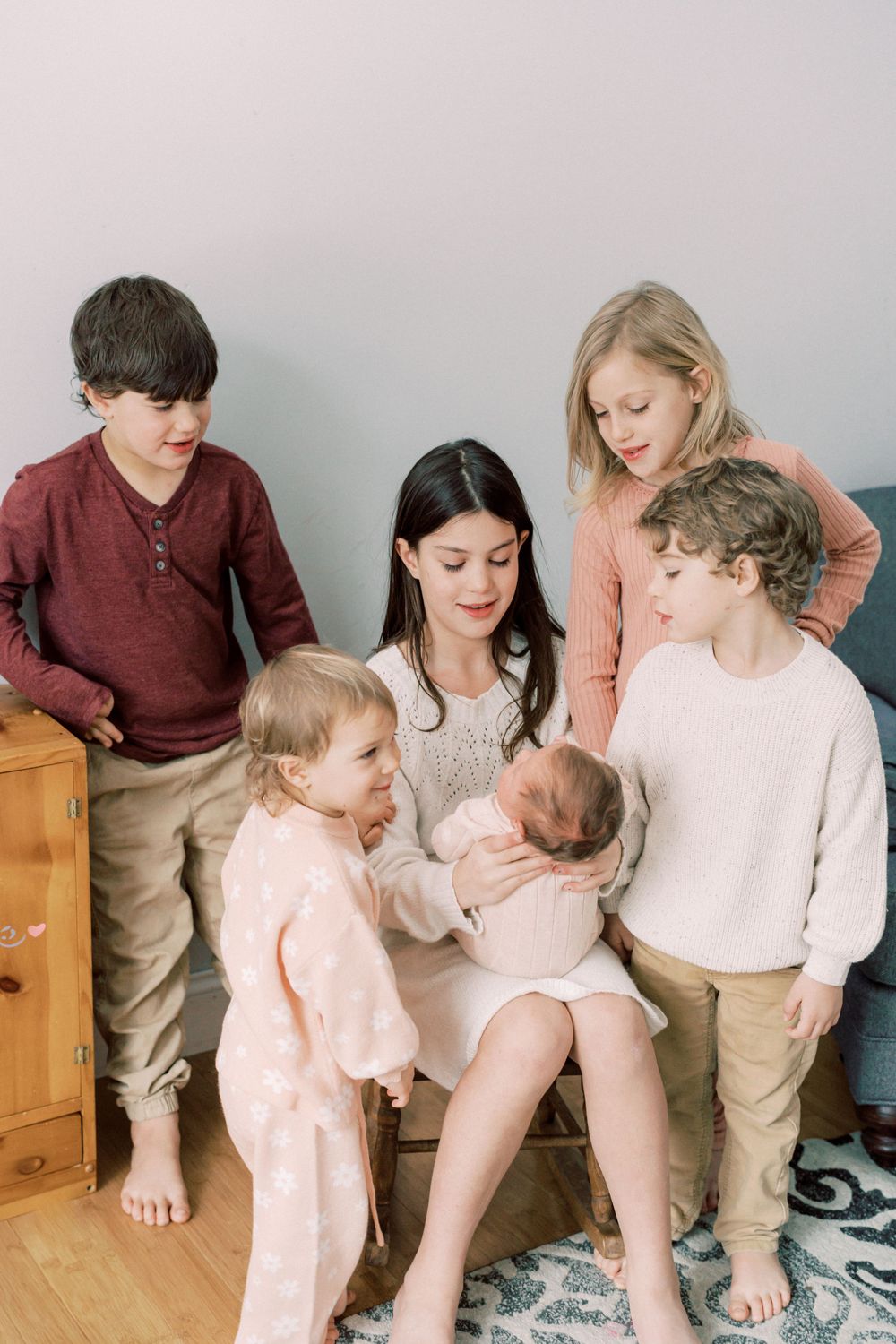 Siblings gathered around their newest family member in a cozy indoor setting.
