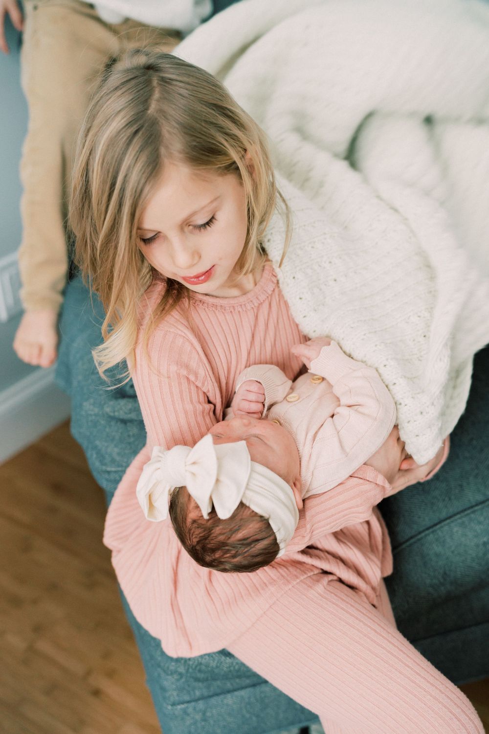 A child in pink holds a newborn baby while sitting on a blue couch.