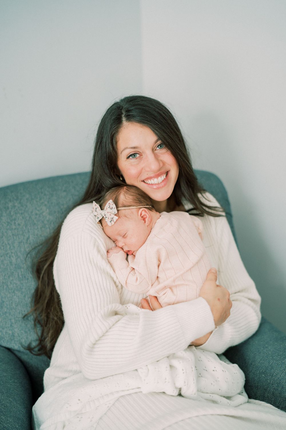 A tender moment between parent and newborn on a blue couch in soft white sweaters.