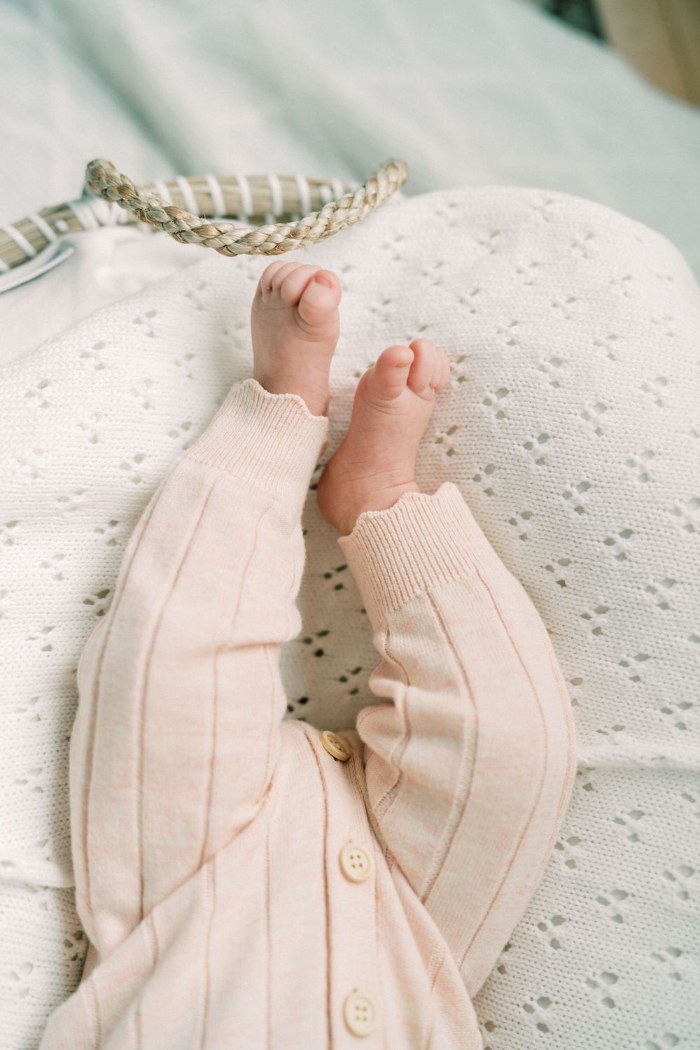 Close-up of tiny baby feet in cream-colored knit clothing against white textured fabric.