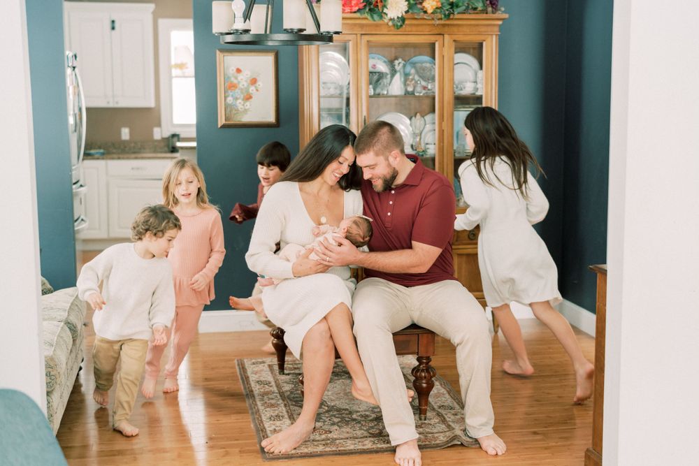 Family moment captured in living room as children play while parents hold newborn.