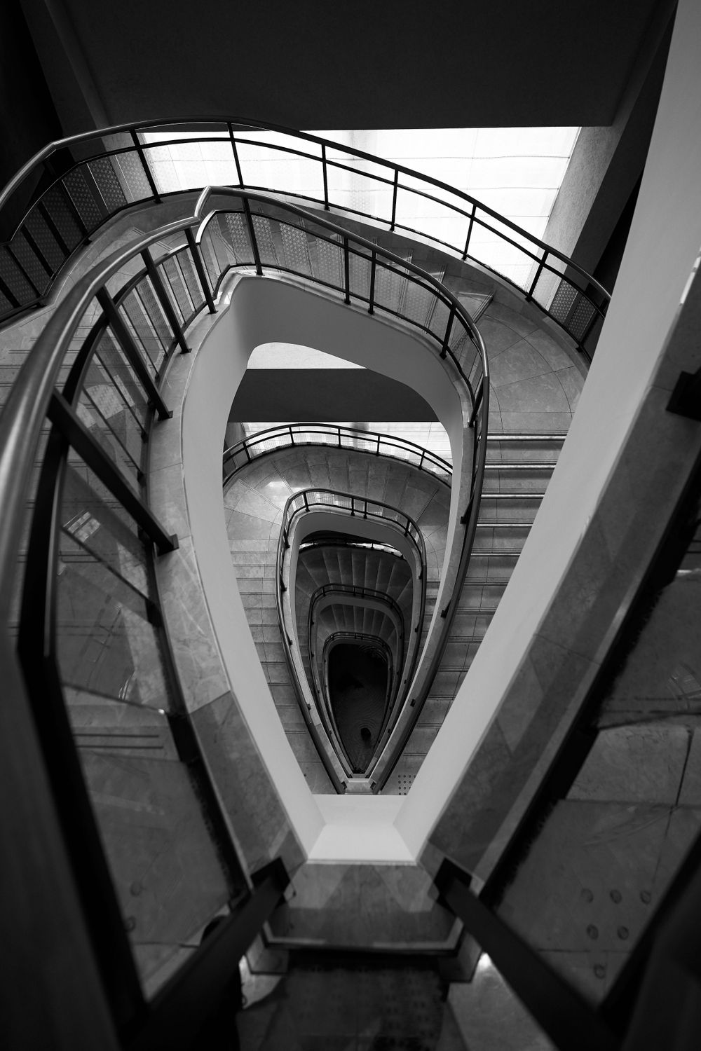 Looking down a dramatic spiral staircase in black and white with curved railings and geometric architectural details.