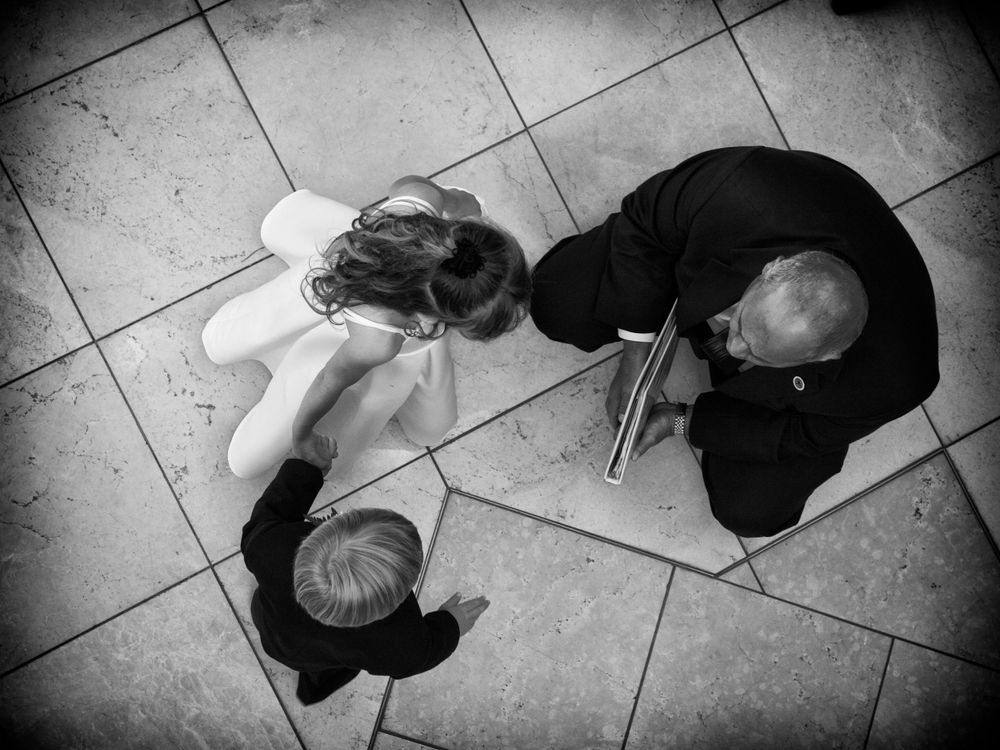 A black and white overhead view of the pastor talking to the flower girl and ring bearer on tile floor captured from above.