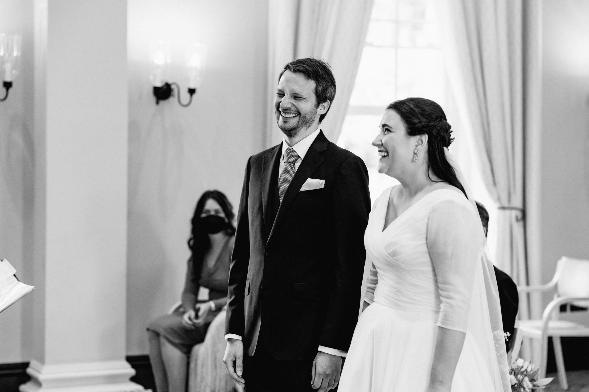 A candid black and white wedding moment captured in an elegant room with wall sconces.
