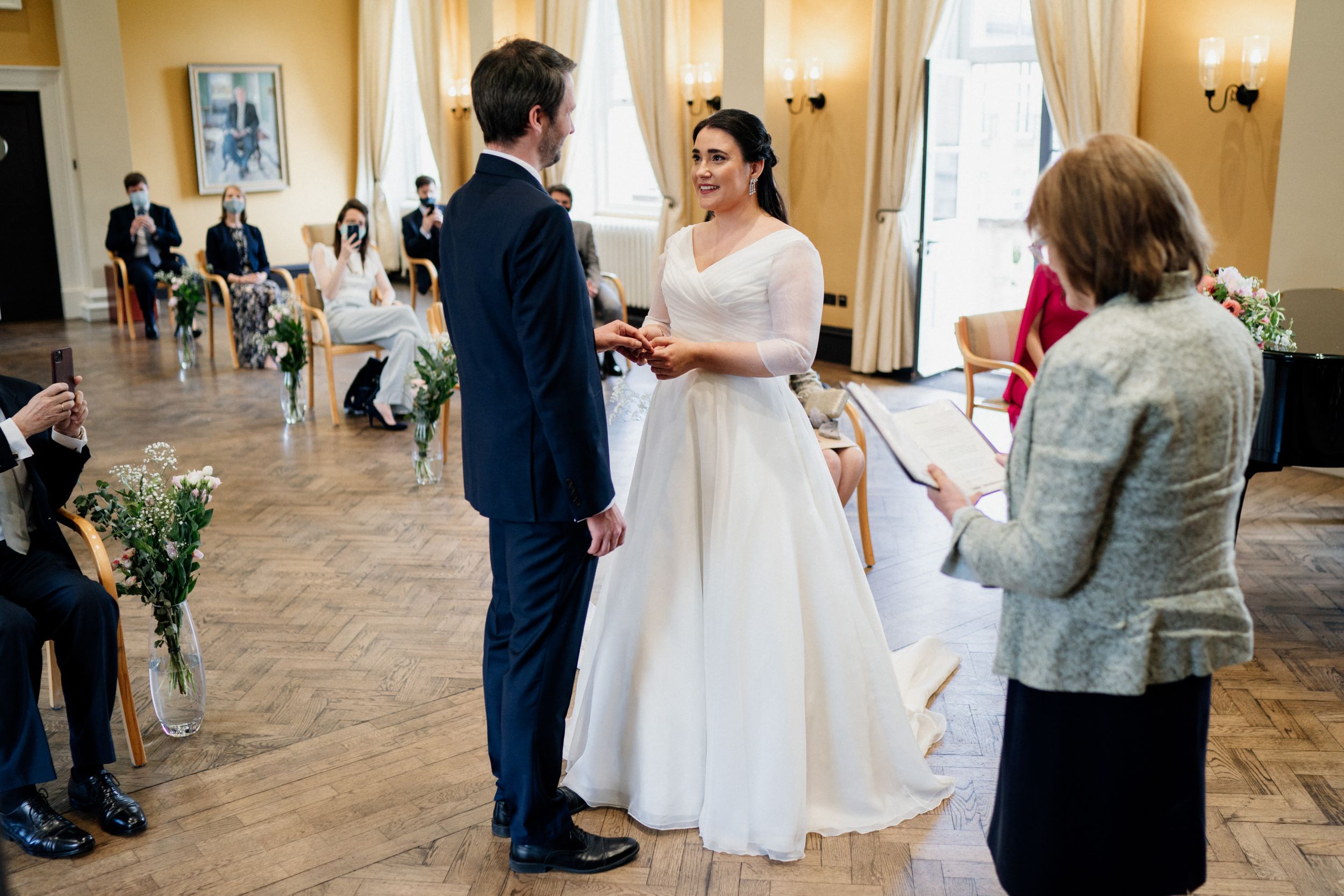 Wedding ceremony in a bright ballroom with guests seated as couple exchanges vows at the altar.