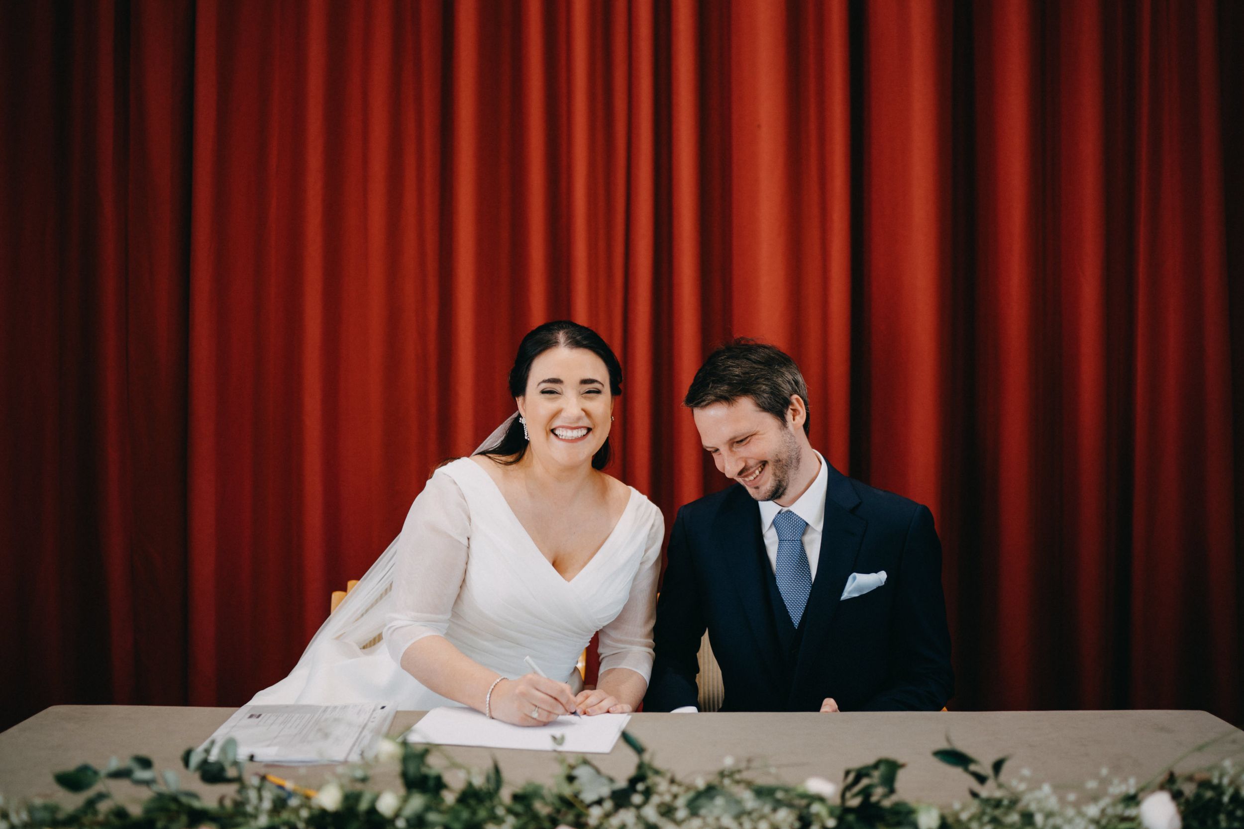 Newlyweds sharing a happy moment while signing documents at a decorated table.