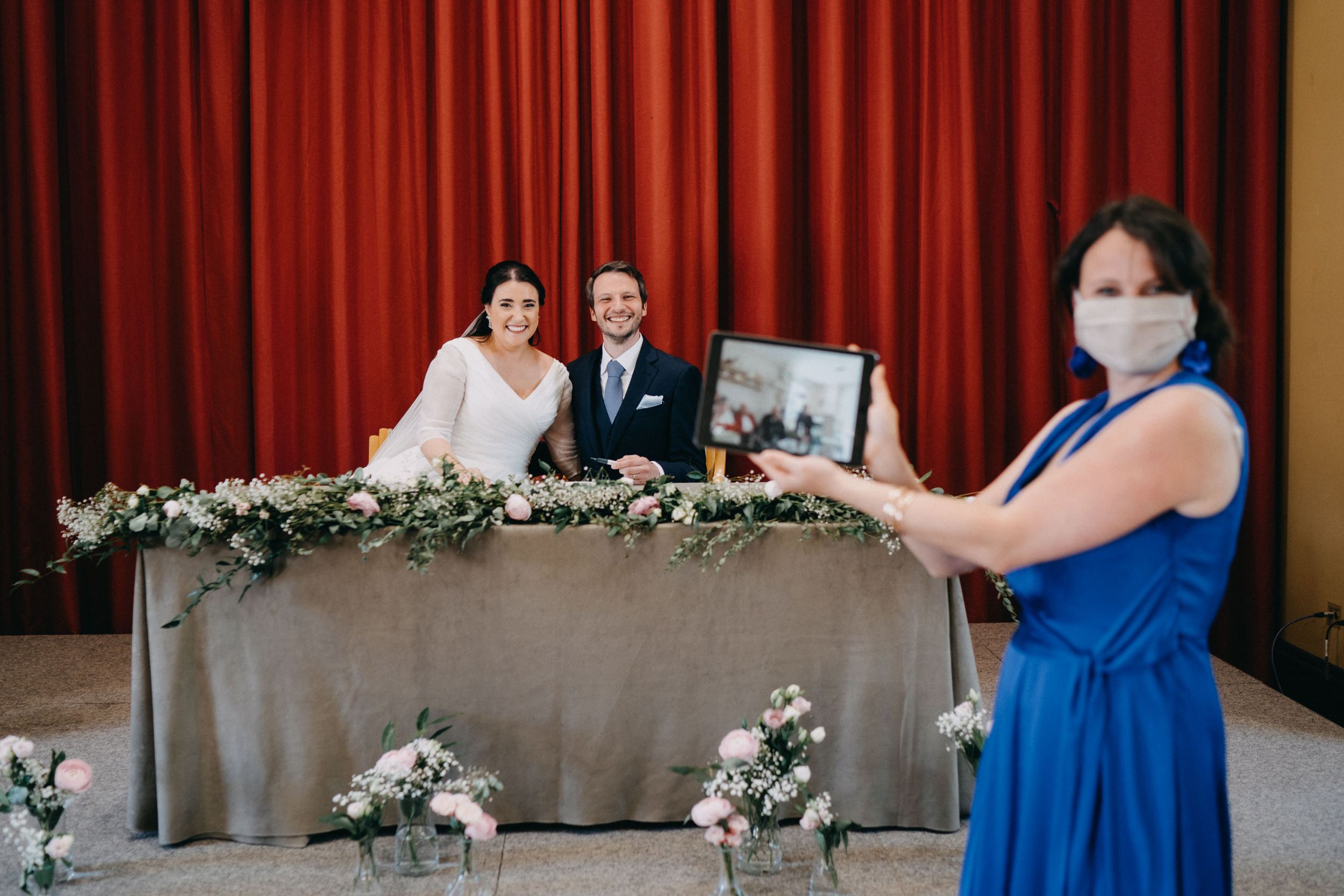 Wedding reception table decorated with greenery garlands and a person in blue holding a photo.