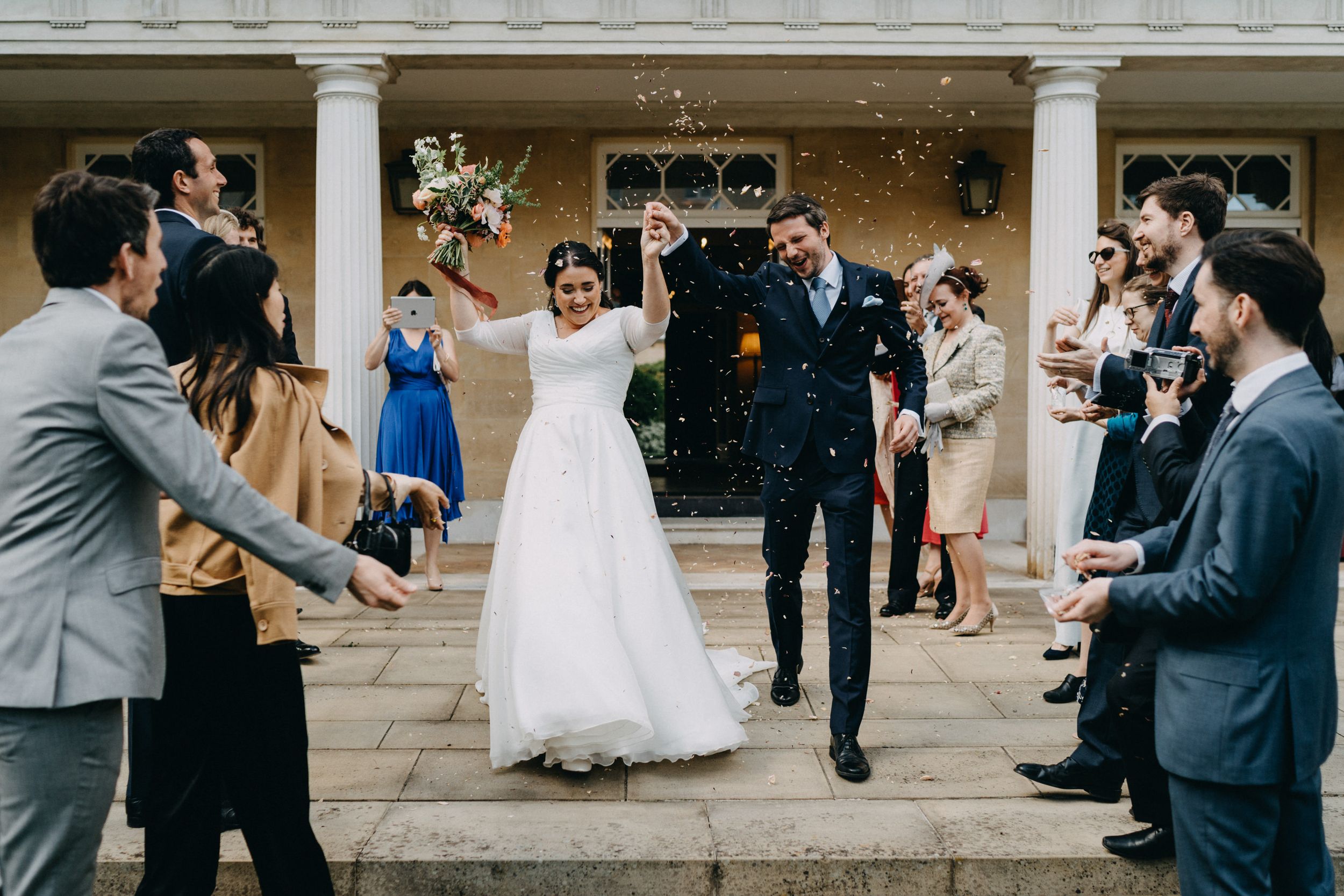 Wedding celebration with guests throwing confetti as couple walks through on stone steps.
