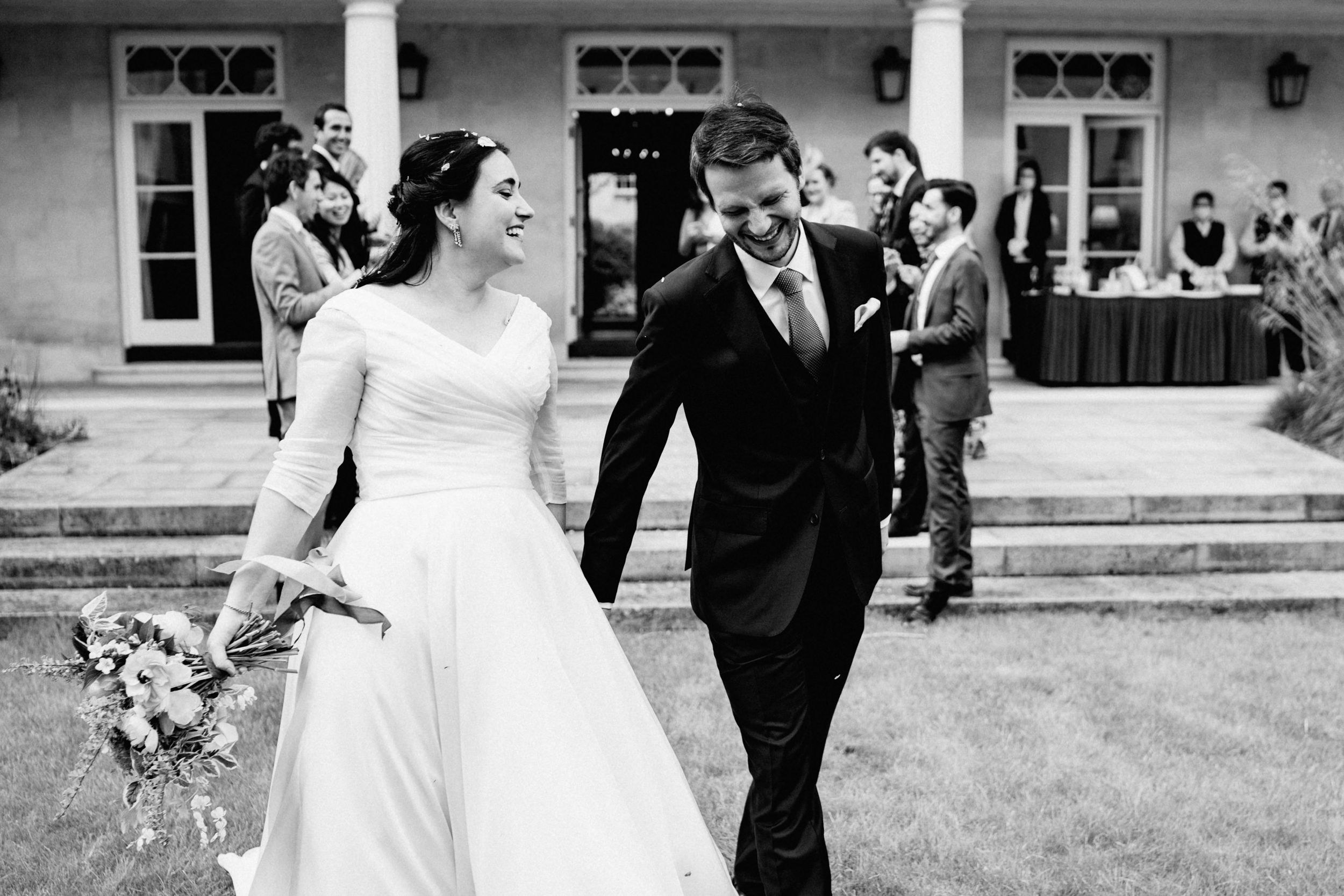 A black and white wedding photo of a couple walking together on a lawn in front of a building.