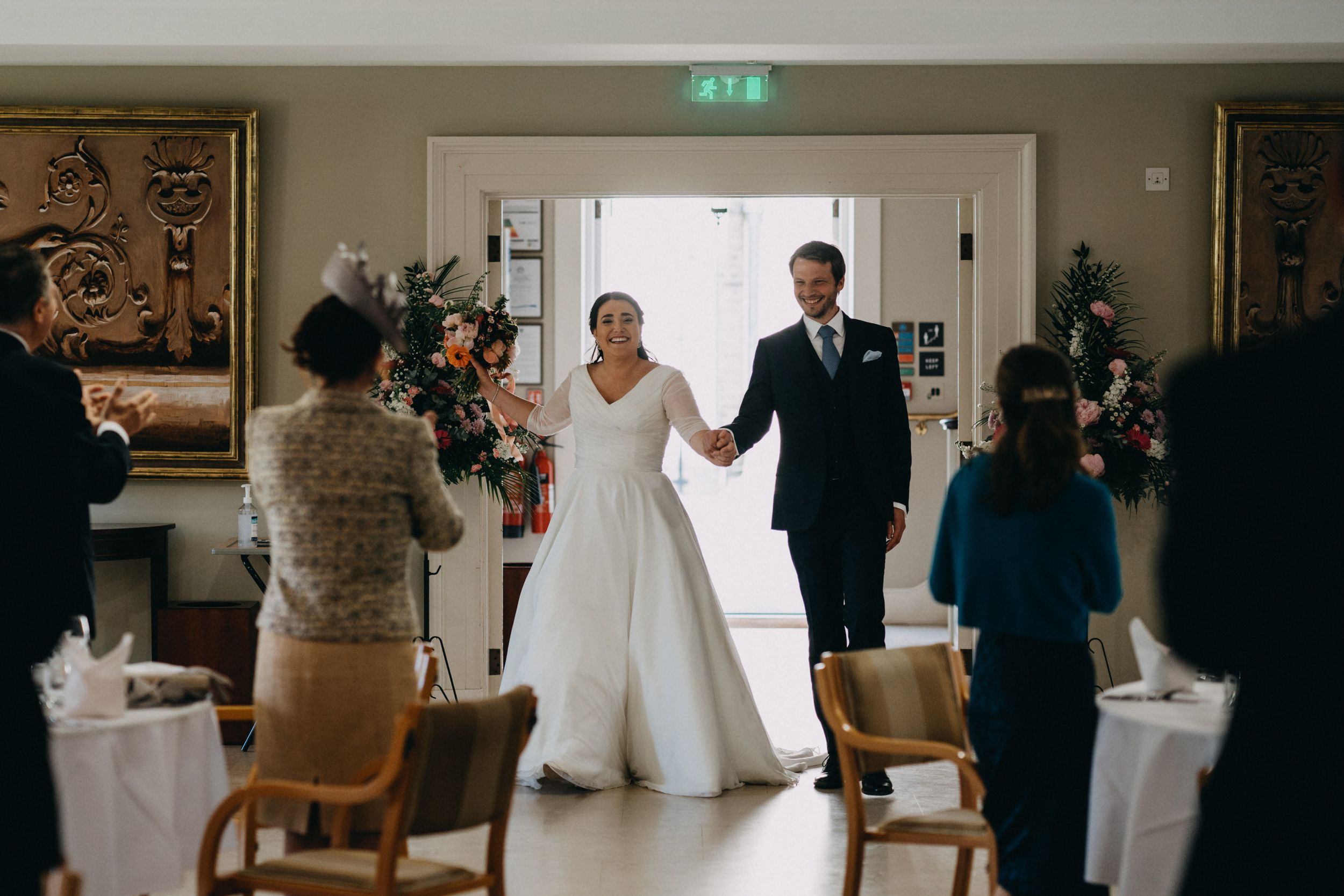 A newlywed couple makes their grand entrance into an elegant reception venue with wood-paneled walls and white linens.