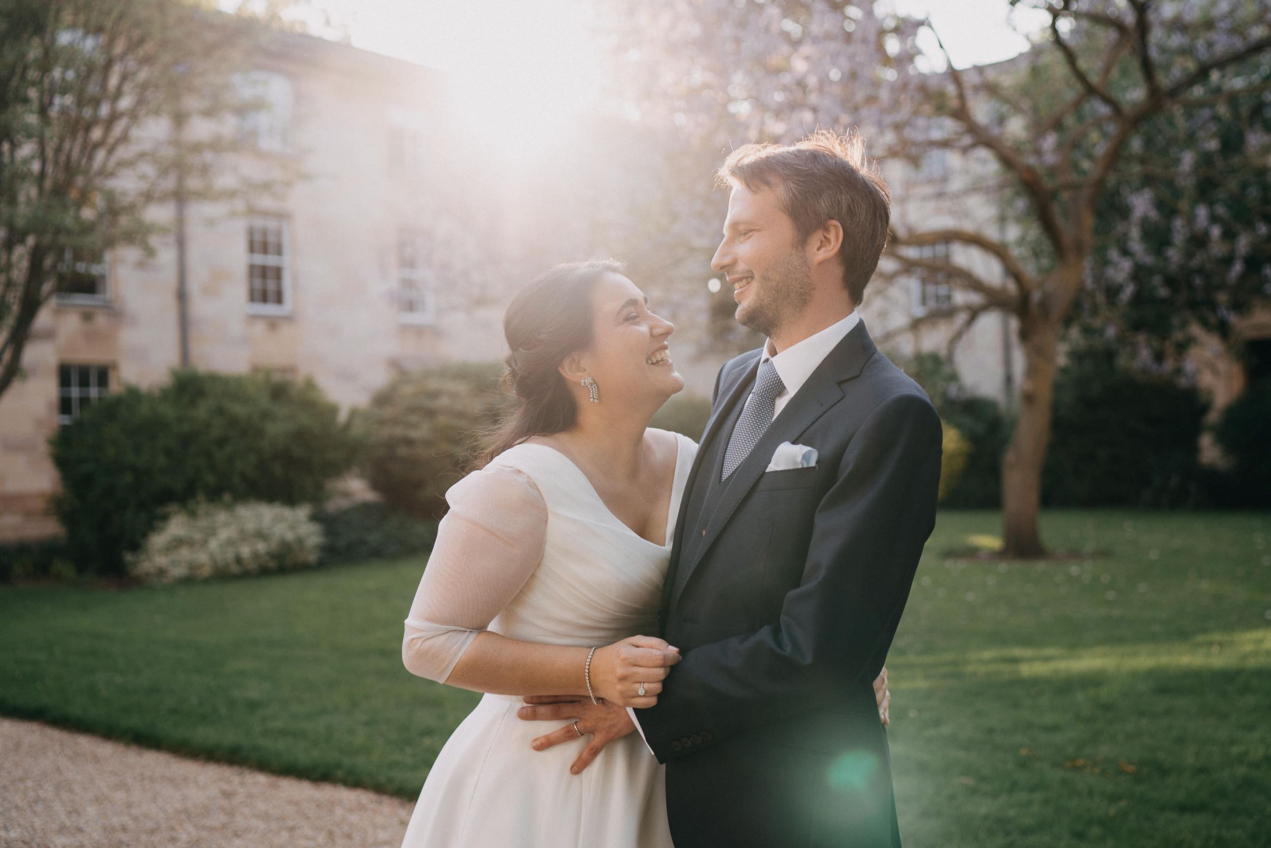 A romantic wedding portrait captured in golden sunlight outside an elegant stone building.