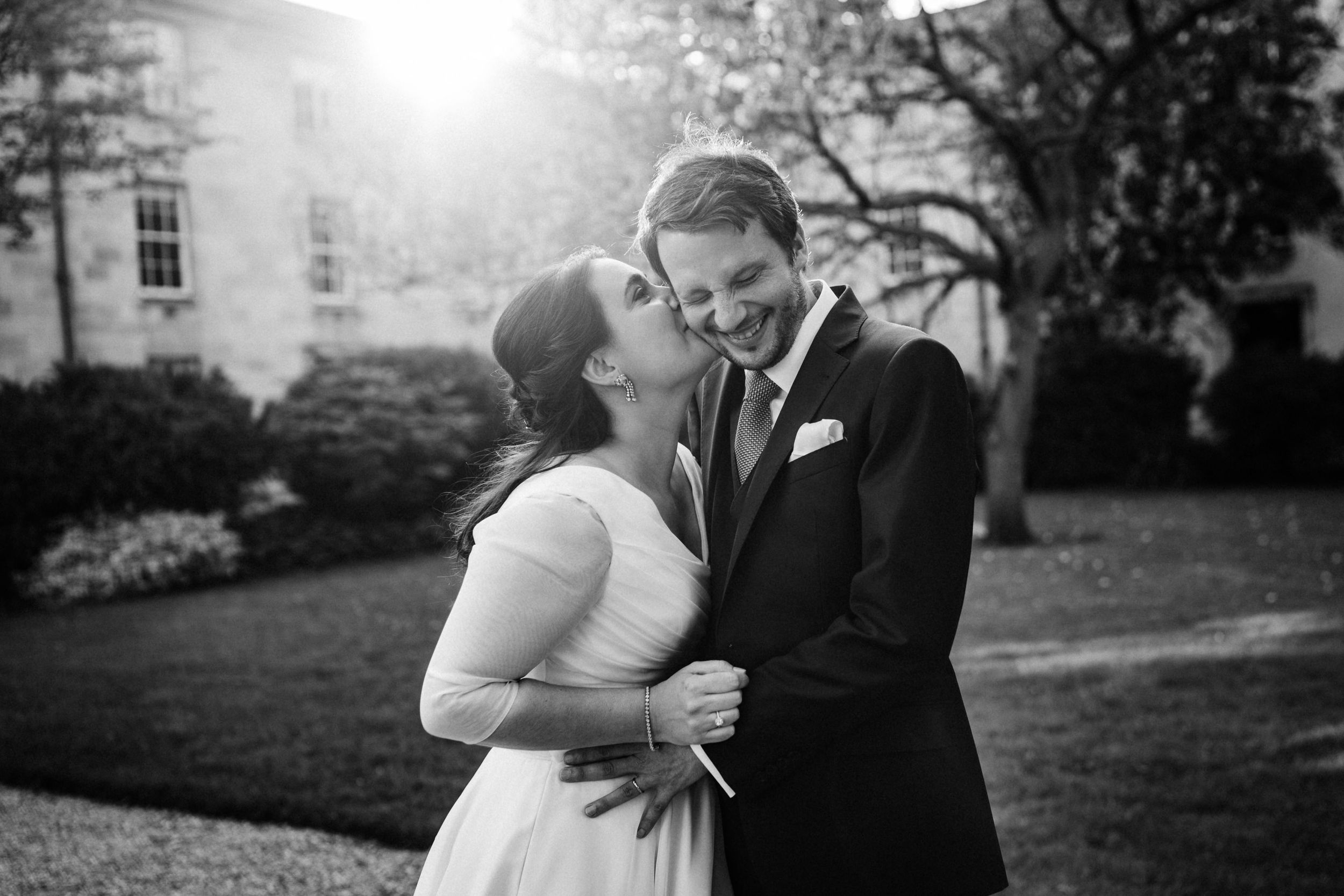 A black and white romantic moment between newlyweds on a manicured lawn with architecture in background.