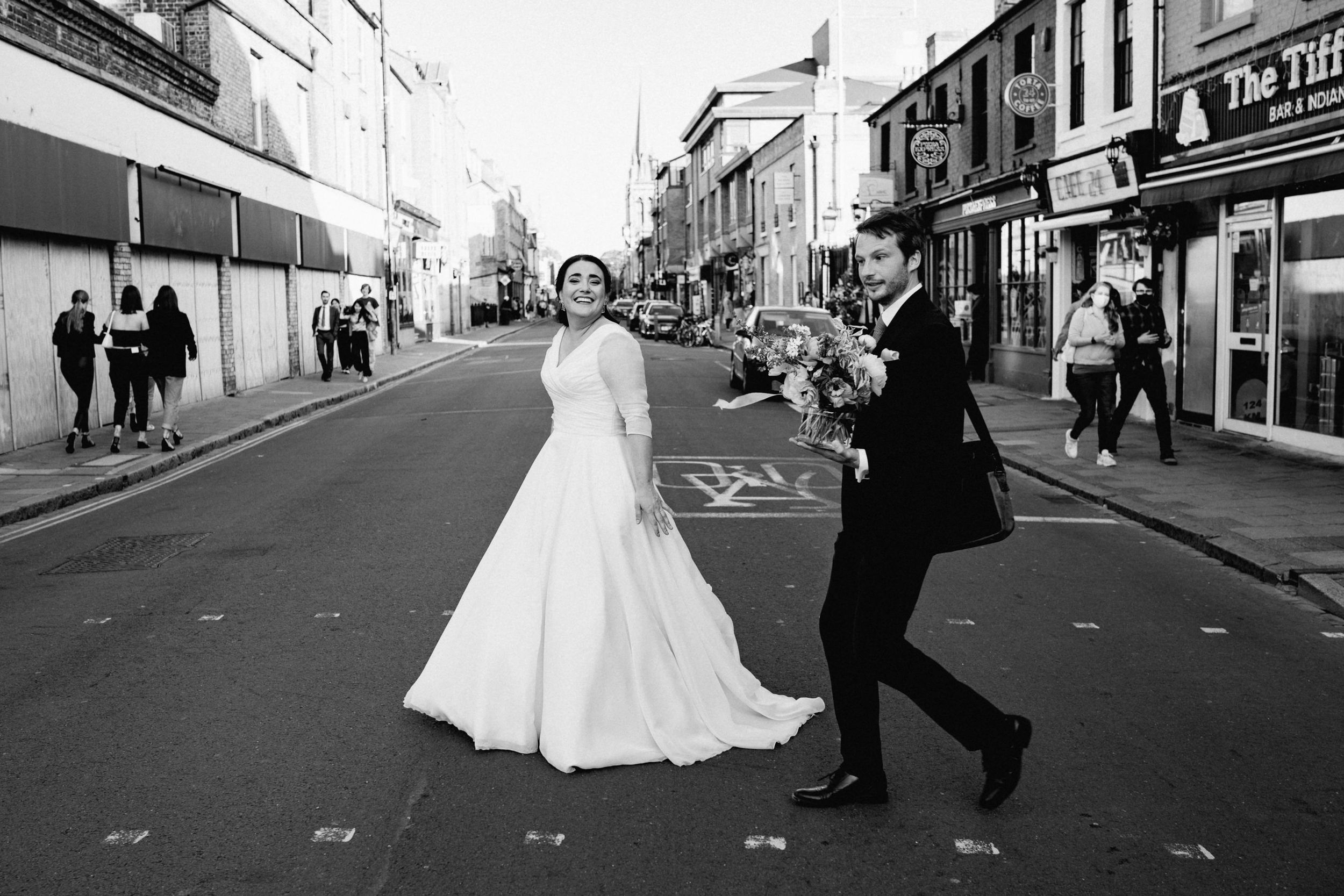 A playful black and white photo of newlyweds dancing in the middle of street in Cambridge.