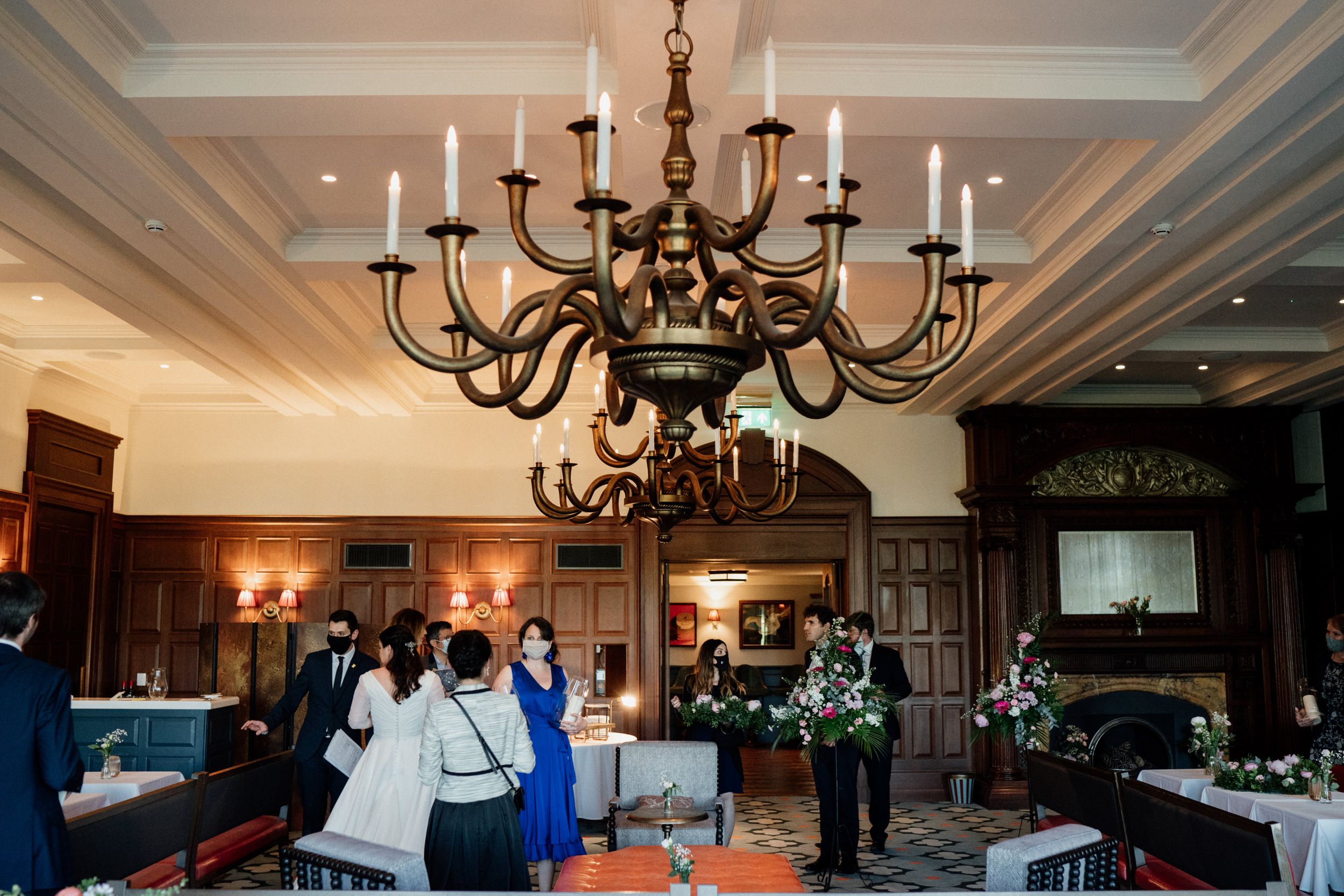 An elegant reception room at University Arms Hotel with dark wood paneling and large black chandeliers hanging from a coffered ceiling.